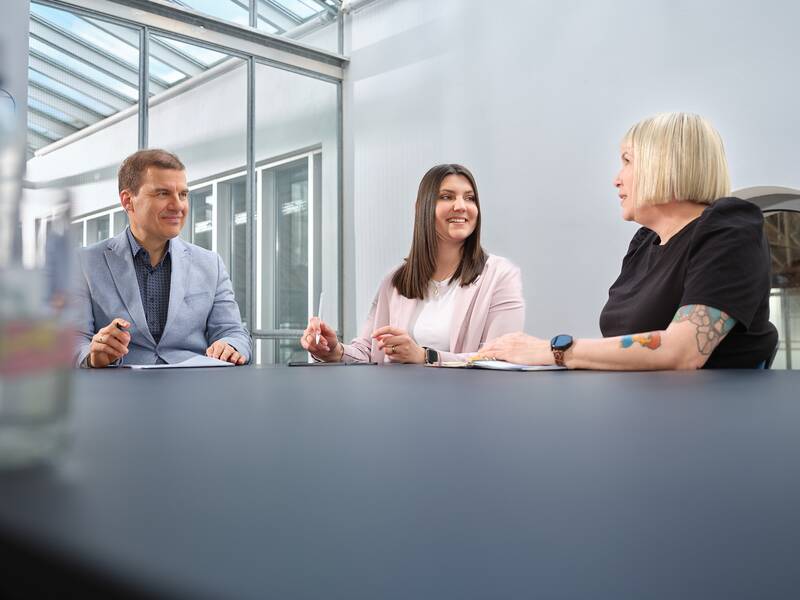 Zwei Frauen und ein Mann sitzen an einem Tisch und sprechen miteinander.