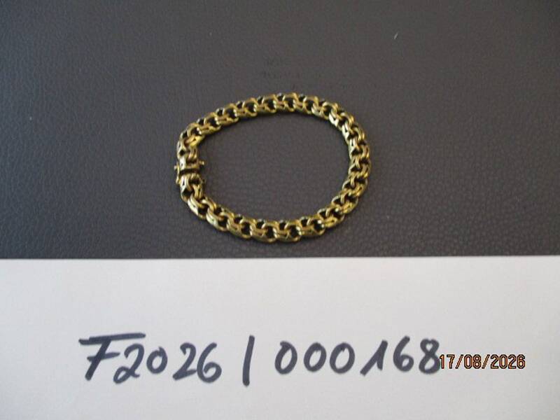 Ein goldfarbenes Kettenglied-Armband liegt auf einer dunklen Oberfläche, darunter sind handschriftliche Zeichen und eine Datumsangabe notiert. KI-BildBeschreiber