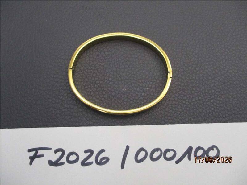 Ein einfacher goldener Armreif liegt auf einer dunklen Oberfläche neben einer Notiz mit der Aufschrift "F2026 1000/100" und einem Datum. KI-BildBeschreiber