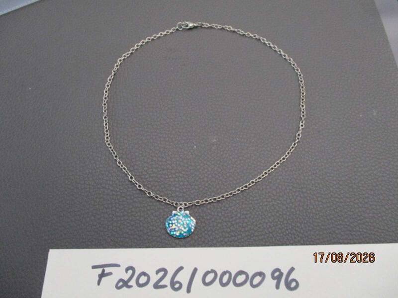 Eine silberne Halskette mit einem runden, glitzernden blauen Anhänger liegt auf einer dunklen Oberfläche, mit der Nummer "F20261/000096" im Vordergrund. KI-BildBeschreiber