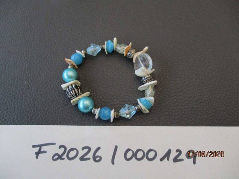 Ein elastisches Armband mit blauen und transparenten Perlen sowie weißen Scheiben liegt auf einer dunkelgrauen Oberfläche; darunter die handgeschriebene Nummer "F20261000129". KI-BildBeschreiber