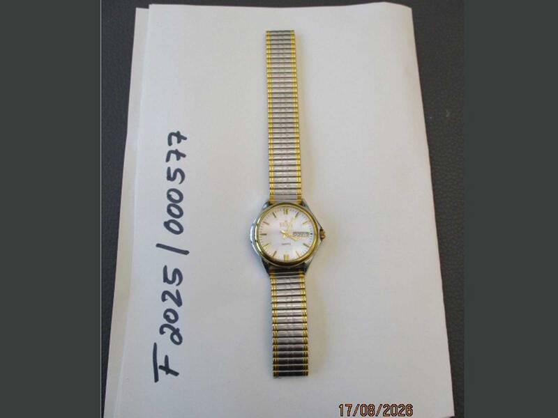 Eine Armbanduhr mit Metallarmband liegt auf einem weißen Blatt Papier, auf dem Zahlen und Buchstaben notiert sind. KI-BildBeschreiber