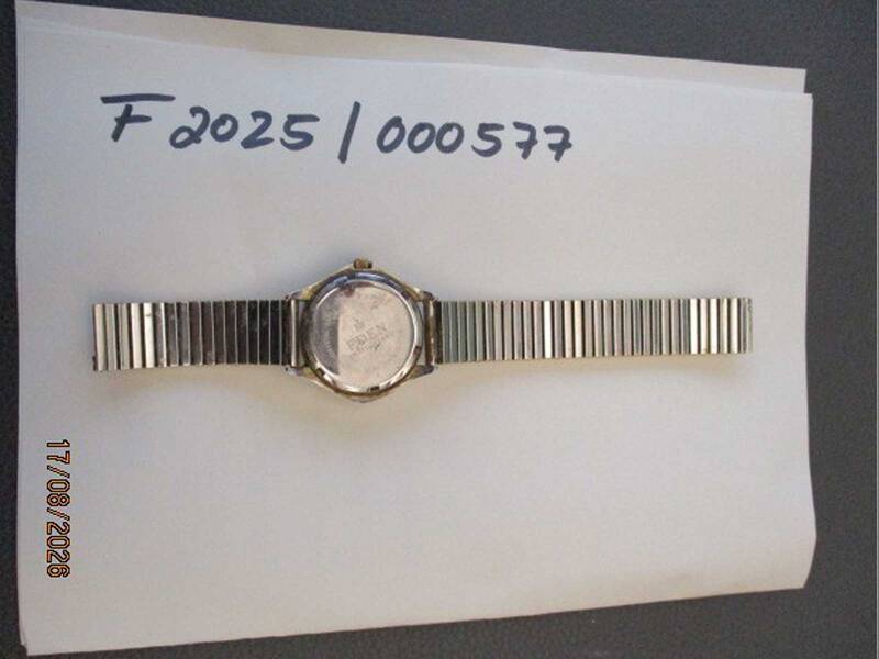 Eine silberne Armbanduhr mit Metallarmband liegt auf einem Blatt Papier mit der Aufschrift "F 2025 / 000577", und das Datum 17/08/2026 ist unten links zu sehen. KI-BildBeschreiber
