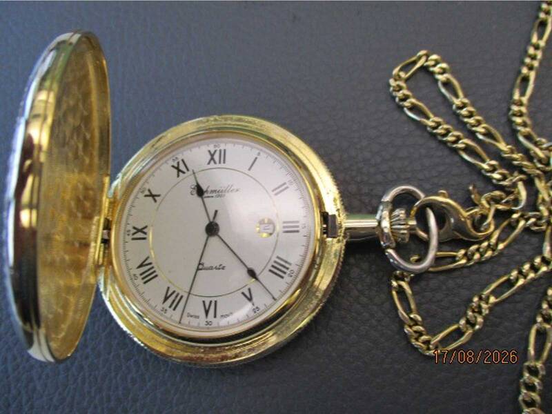 Eine offene, goldene Taschenuhr mit römischen Ziffern und einer Kette liegt auf einer dunklen Oberfläche. KI-Bildbeschreiber