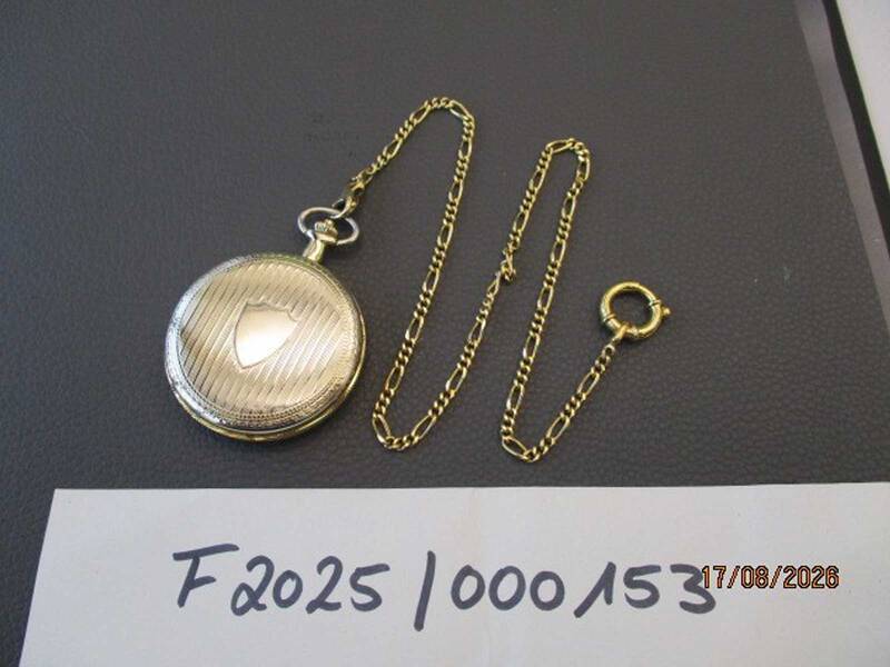 Eine goldene Taschenuhr mit Kette liegt auf einer Oberfläche, daneben steht eine handschriftliche Notiz mit der Nummer "F2025/000153" und dem Datum "17/08/2026". KI-BildBeschreiber