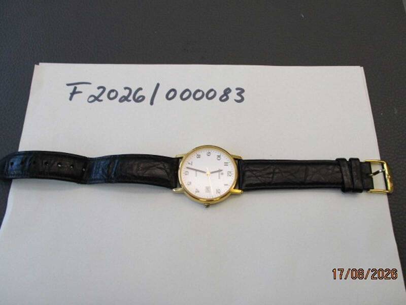 Eine goldene Armbanduhr mit schwarzem Lederarmband liegt auf einem Papier, das mit "F2026/000083" beschriftet ist. KI-BildBeschreiber