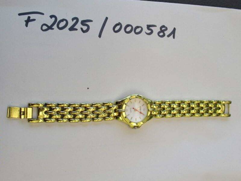 Eine goldene Armbanduhr mit weißem Zifferblatt liegt auf einer Oberfläche, oberhalb steht handgeschrieben "F2025/000581".