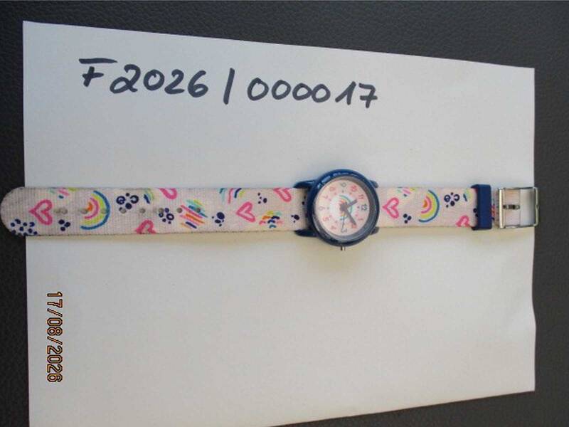 Eine bunte Kinderarmbanduhr mit Herz- und Regenbogenmotiven liegt auf einem weißen Blatt Papier, das mit "F2026 | 000017" beschriftet ist. KI-BildBeschreiber