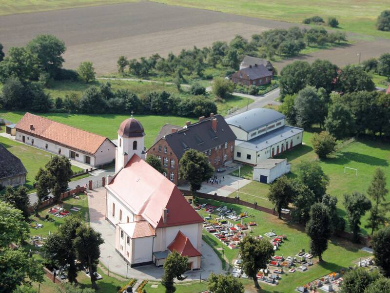Zu sehen sind eine Kirche mit Friedhof und weitere Gebäude in einer ländlichen Umgebung. 
