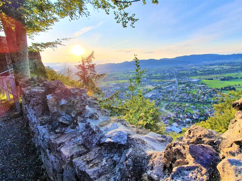 Ein Weg entlang einer alten Steinmauer bietet einen malerischen Blick auf eine weitläufige Landschaft mit einer Stadt im Sonnenuntergang.