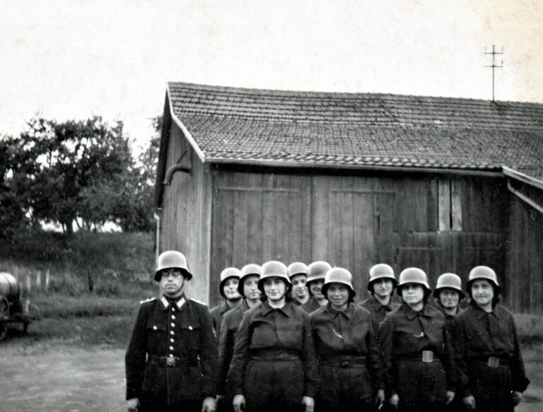Frauengruppe Feuerwehr Nellingen Eine Gruppe uniformierter Frauen und ein uniformierter Mann stehen vor einem Holzhäuschen.