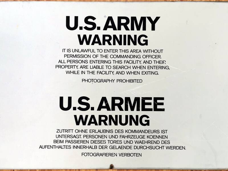 Ein Schild der US-Armee mit Warnhinweisen in Englisch und Deutsch, das den Zutritt ohne Erlaubnis verbietet und das Fotografieren untersagt.