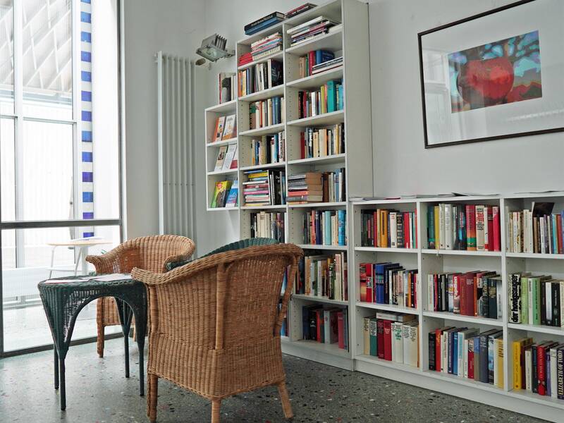 ImTreffpunkt An der Halle stehen vor einer Bücherwand ein Tisch und zwei Korbstühle