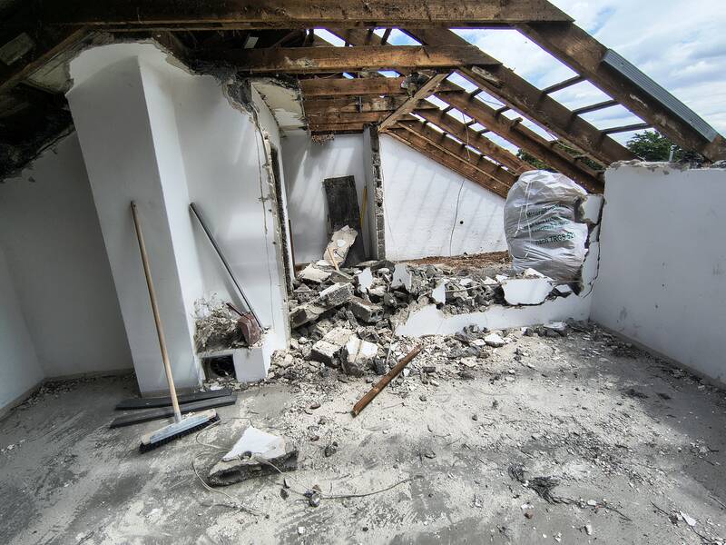 Eine teilweise abgerissene Dachkonstruktion mit sichtbaren Holzbalken und Bauschutt auf dem Boden.