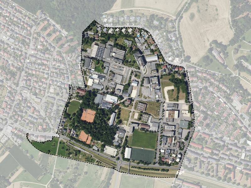 Das Bild zeigt eine Luftaufnahme des Gebietes Zinsholz mit klar abgegrenzten Strukturen, darunter Gebäude, Grünflächen und Straßen, umgeben von einer gepunkteten Linie, die den Bereich hervorhebt.