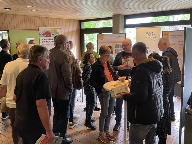 Mehrere Menschen versammeln sich in einem Raum vor Informationsständen zu kommunalem Wärmepan und Klimaschutz.