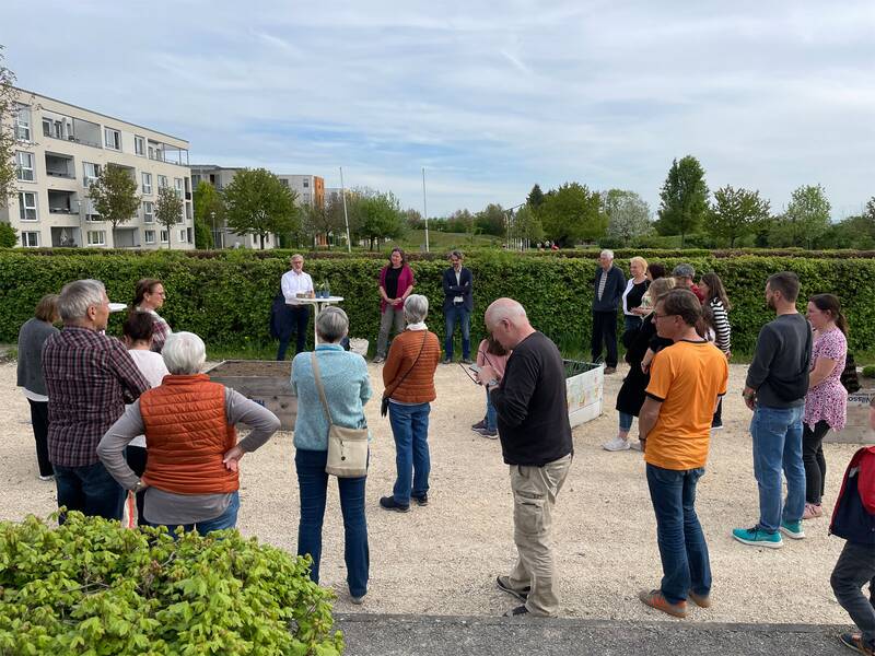Eine Gruppe von Menschen steht im Freien zusammen, während jemand in der Mitte eine Rede hält.