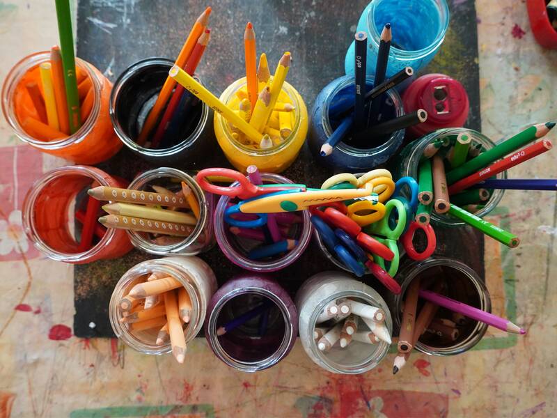 Eine Sammlung von bunt gemischten Buntstiften und Scheren in verschiedenen Gläsern, die von oben betrachtet werden. (KI generiert)