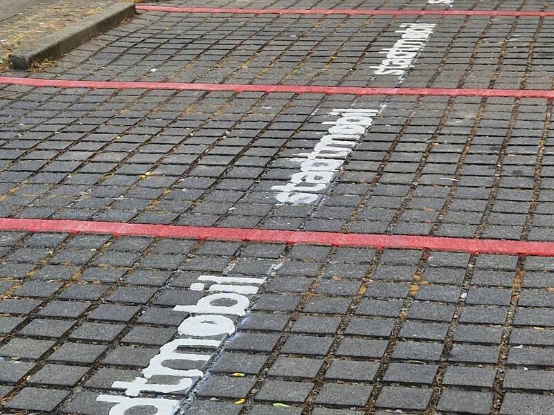 Ein Parkplatz mit mehreren Stellplätzen, auf denen "stadtmobil" in weißer Schrift auf dem grauen Kopfsteinpflaster steht, ist zu sehen.