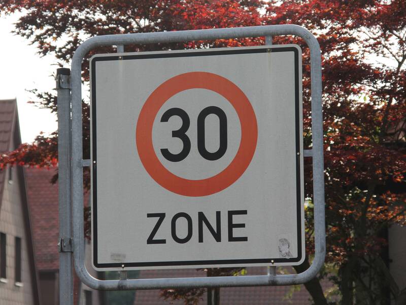 Ein Verkehrsschild mit der Aufschrift "30 Zone" vor einem Baum im Hintergrund.