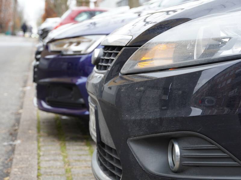 Nahaufnahme mehrerer hintereinander geparkter Autos am Straßenrand in einer städtischen Umgebung.