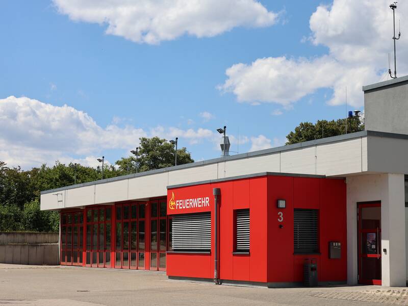 Das Bild zeigt das Feuerwehrgebäude in Nellingen mit roten und grauen Wänden an einem sonnigen Tag.
