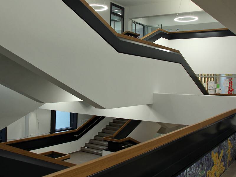 Das moderne Treppenhaus mit verschachtelten Treppen und hölzernen Handläufen im Otto-Hahn-Gymnasium.