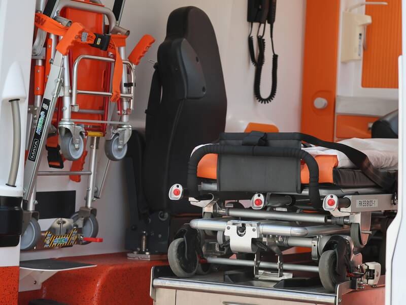 Der Innenraum eines Krankenwagens zeigt eine Trage und einen zusammenklappbaren Transportstuhl in Orange und Metallic.