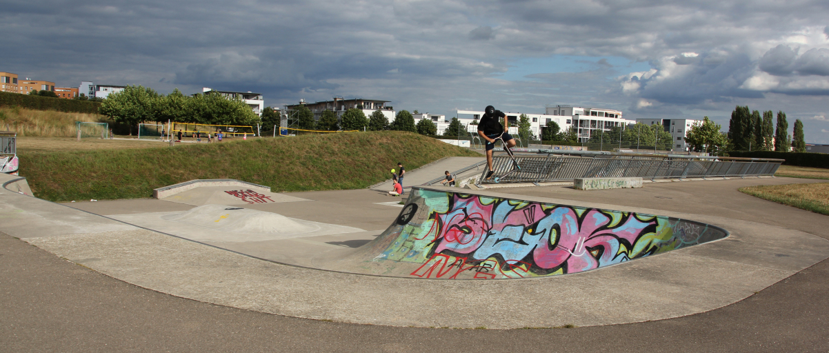 Über Rampen, die mit bunten Graffiti besprüht wurden, fahren Jugendliche mit Rollern und Skateboards.