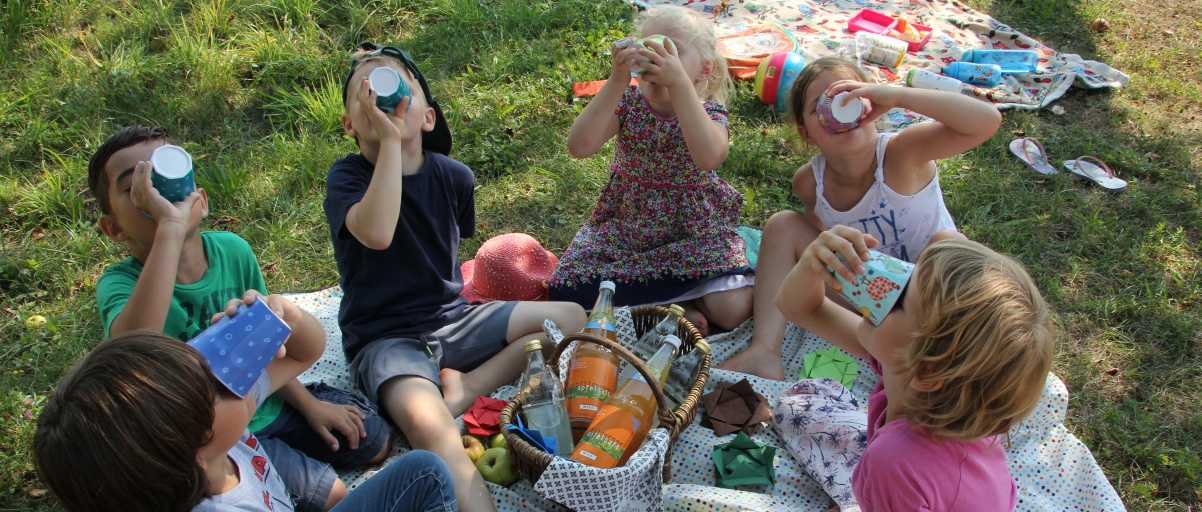 Kinder sitzen auf einer Picknickdecke und trinken Ostfilderner Apfelsaft