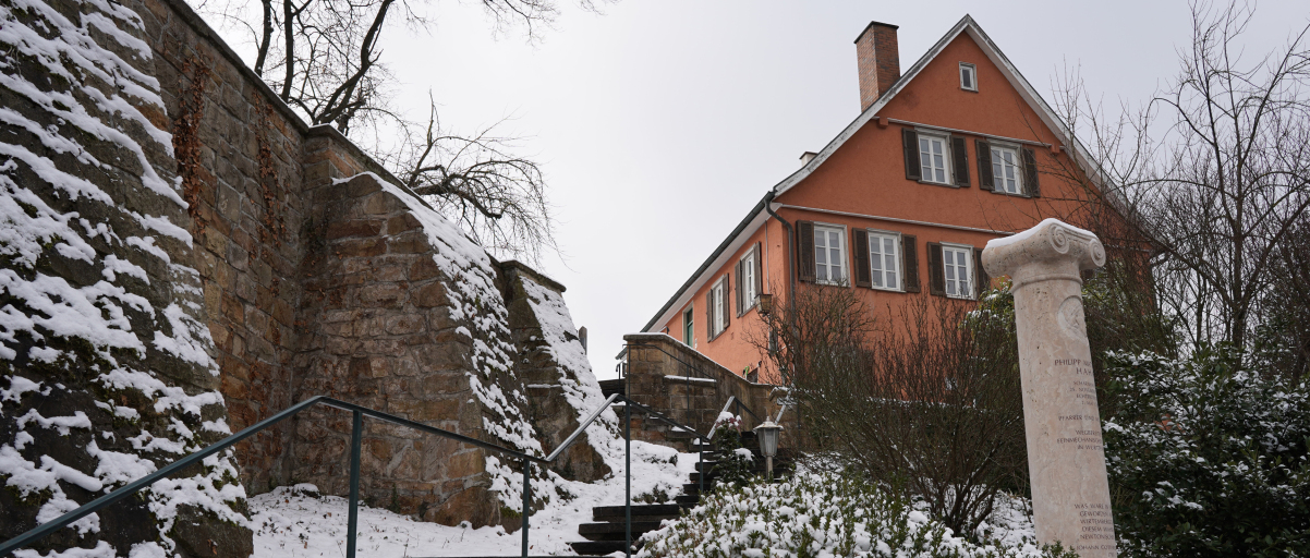 Das evangelische Pfarrhaus in Scharnhausen im Winter. Unterhalb ist die Stele zu sehen, die an Philipp Matthäus Hahn erinnert.