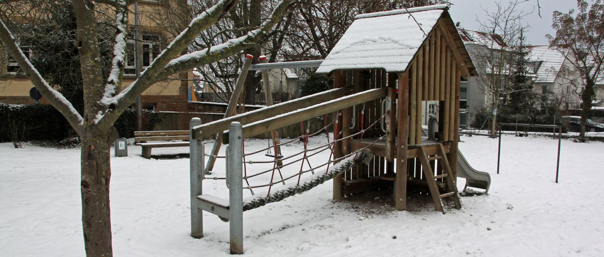 Ein Kinderspielhaus aus Holz steht auf einer schneebedeckten Wiese.