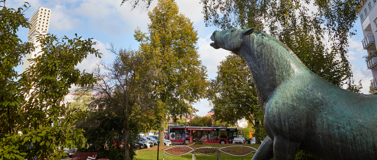 Im Vordergrund ist die Statue in Form eines Pferdes zu sehen. Im Hintergrund der Turm der evangelischen Kirche im Stadtteil Parksiedlung.