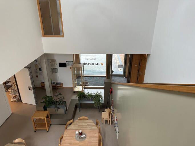 Bild zeigt das Foyer im Erdgeschoss, unten ist der Eingangsbereich zu sehen. Blick von oben auf die Pflanzen, Regale, Tische und Stühle.