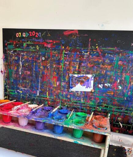 Blick auf ein buntes Kunstwerk, davor stehen Behälter mit unterschiedlichen Farben